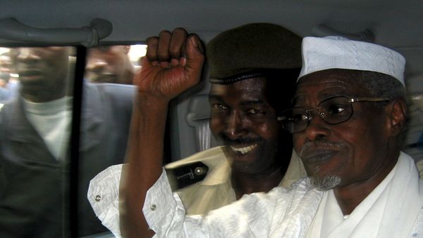 Former Chad President Hissene Habre (R) raises his fist in the air as he leaves a court in Dakar escorted by a Senegalese policeman in this November 25, 2005 file photo - Sputnik International