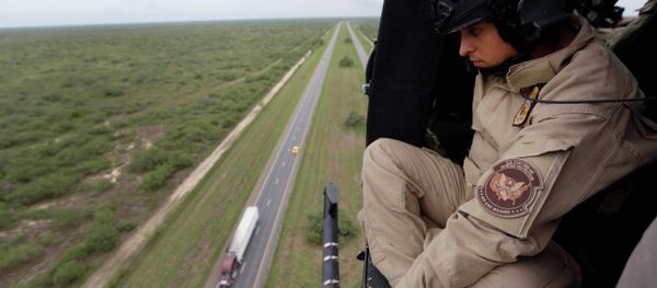 A US Customs and Border Protection Air and Marine agent pears out of the open door of a helicopter during a patrol flight near the Texas-Mexico border. A US Customs and Border Protection Air and Marine agent pears out of the open door of a helicopter during a patrol flight near the Texas-Mexico border. - Sputnik International