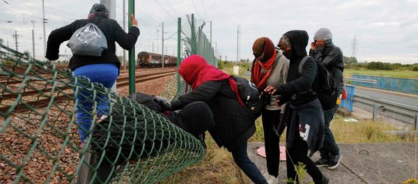 Migrants make their way across a fence near train tracks Migrants make their way across a fence near train tracks - Sputnik International