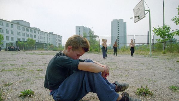 A boy sits by himself on the playground as other boys play in the background. - Sputnik International