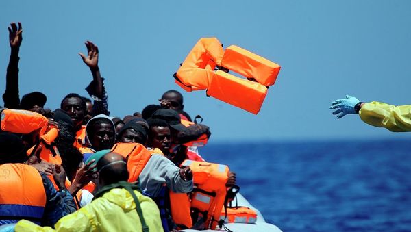 A Belgian nav.y sailor passes life vests to migrants sitting in a rubber boat as they approach the Belgian Navy Vessel Godetia during a search and rescue mission in the Mediterranean Eea off the Libyan coasts, Tuesday, June 23, 2015 - Sputnik International