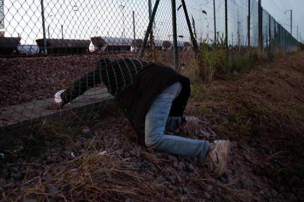 A migrant crawls under a fence as he attempts to access the Channel Tunnel in Calais, northern France, Saturday, Aug. 8, 2015 - Sputnik International