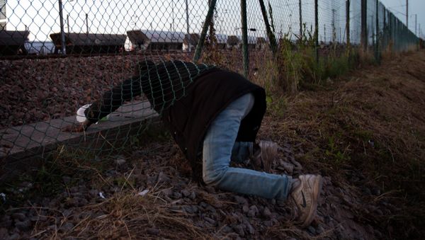 A migrant crawls under a fence as he attempts to access the Channel Tunnel in Calais, northern France, Saturday, Aug. 8, 2015 A migrant crawls under a fence as he attempts to access the Channel Tunnel in Calais, northern France, Saturday, Aug. 8, 2015 - Sputnik International