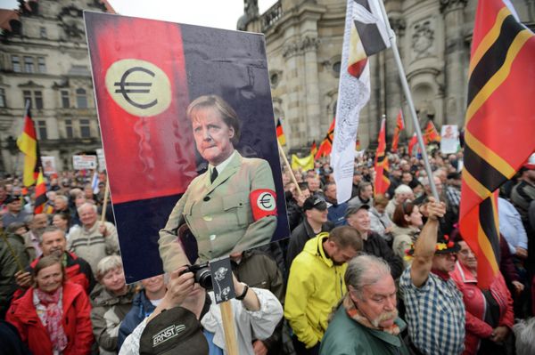 Supporters of the German right-wing movement PEGIDA (Patriotic Europeans Against the Islamisation of the Occident) hold up a poster showing German Chancellor Angela Merkel in a uniform with an Euro-logo-armband as they attend a PEGIDA rally on June 1, 2015 in Dresden, eastern Germany. Supporters of the German right-wing movement PEGIDA (Patriotic Europeans Against the Islamisation of the Occident) hold up a poster showing German Chancellor Angela Merkel in a uniform with an Euro-logo-armband as they attend a PEGIDA rally on June 1, 2015 in Dresden, eastern Germany. - Sputnik International