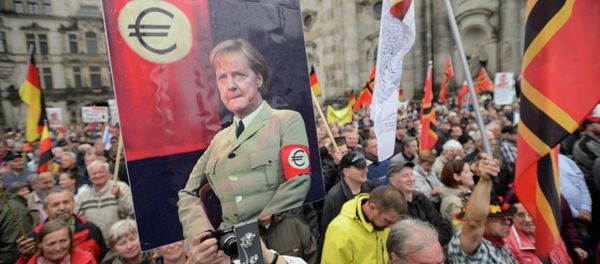 Supporters of the German right-wing movement PEGIDA (Patriotic Europeans Against the Islamisation of the Occident) hold up a poster showing German Chancellor Angela Merkel in a uniform with an Euro-logo-armband as they attend a PEGIDA rally on June 1, 2015 in Dresden, eastern Germany. - Sputnik International