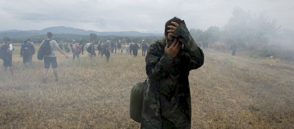 A migrant covers his face to avoid inhaling tear gas while others flee, as Macedonian police special forces block them from entering Macedonia on Greece's, near the village of Idomeni, Greece, August 22, 2015. - Sputnik International