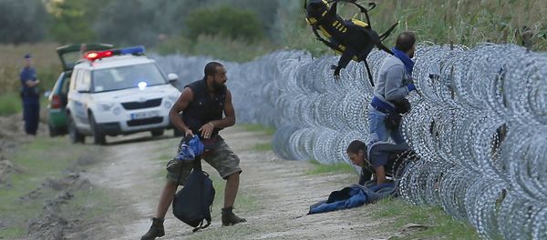 Hungarian police positioned nearby watch as Syrian migrants climb under a fence to enter Hungary at the Hungarian-Serbian border near Roszke, Hungary August 26, 2015 - Sputnik International