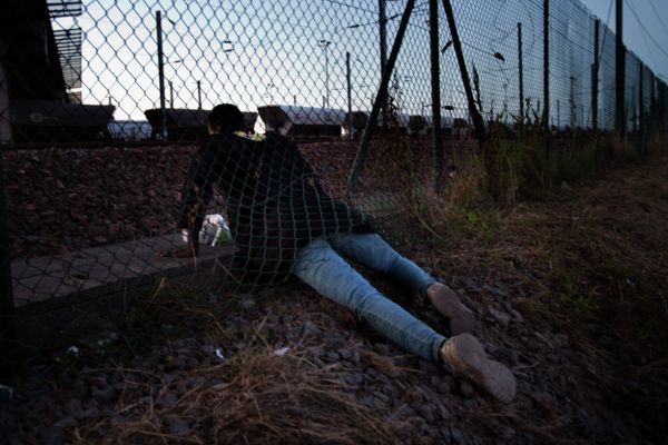A migrant crawls under a fence as he attempts to access the Channel Tunnel in Calais, northern France, Saturday, Aug. 8, 2015. Some thousands of migrants have been crossing fence border controls near the Channel Tunnel linking France and Britain, trying to board freight trains or trucks destined for Britain - Sputnik International