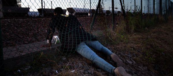 A migrant crawls under a fence as he attempts to access the Channel Tunnel in Calais, northern France, Saturday, Aug. 8, 2015. Some thousands of migrants have been crossing fence border controls near the Channel Tunnel linking France and Britain, trying to board freight trains or trucks destined for Britain A migrant crawls under a fence as he attempts to access the Channel Tunnel in Calais, northern France, Saturday, Aug. 8, 2015. Some thousands of migrants have been crossing fence border controls near the Channel Tunnel linking France and Britain, trying to board freight trains or trucks destined for Britain - Sputnik International