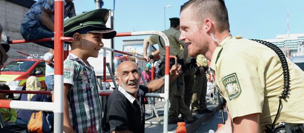 German police officer and a migrant boy joke with the officer's cap while migrants wait for a bus after their arrival at the main train station in Munich, southern Germany, September 1, 2015 German police officer and a migrant boy joke with the officer's cap while migrants wait for a bus after their arrival at the main train station in Munich, southern Germany, September 1, 2015 - Sputnik International