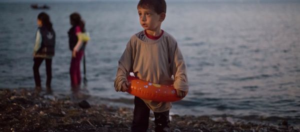A Syrian migrant boy still wearing a swimming ring stands on the beach upon his arrival with other migrants by a dinghy at the southeastern Greek island of Kos, Greece, early Thursday, Aug. 20, 2015. - Sputnik International