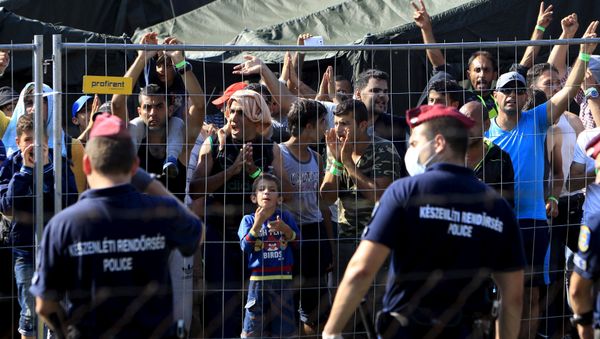 Migrants watch from behind a fence as Hungarian riot police stands guard in front of a migrant reception centre in Roszke, Hungary, September 4, 2015 - Sputnik International