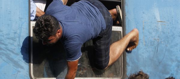 A migrant tries to board a train towards Serbia through a window, at the railway station in the southern Macedonian town of Gevgelija, on Saturday, Aug. 15, 2015 - Sputnik International