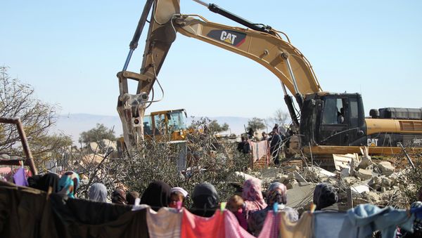 Palestinian women watch on as an Israeli army bulldozer with a demolition permit pulls down a house in the West Bank. - Sputnik International