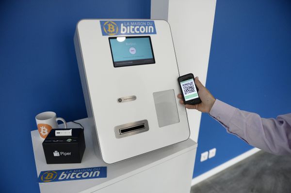 This picture taken on June 20, 2014, shows a man placing his phone next to a Bitcoins (virtual currency) dispenser at La Maison du Bitcoin in Paris. - Sputnik International
