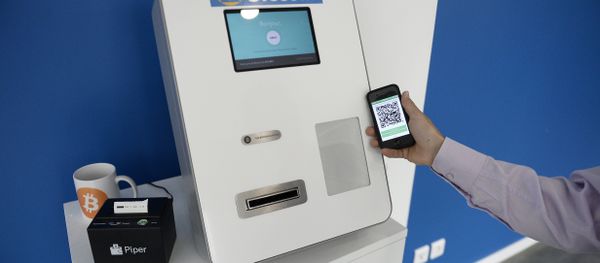This picture taken on June 20, 2014, shows a man placing his phone next to a Bitcoins (virtual currency) dispenser at La Maison du Bitcoin in Paris. - Sputnik International