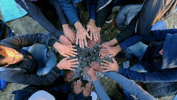 Refugees warm up their hands over hot ash from a bonfire at migrant collection point near Roszke village of the Hungarian-Serbian border on September 8, 2015 - Sputnik International
