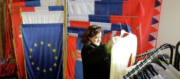 In this photo taken Wednesday, Dec. 7, 2011, a woman looks at an item of clothing in a shop as she stands next to a European Union flag and Serbian flags, in Belgrade, Serbia - Sputnik International