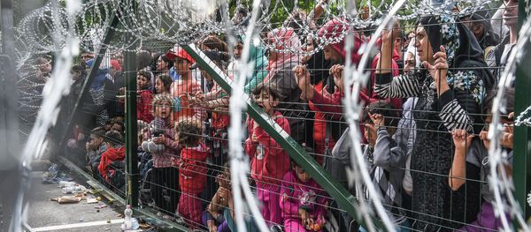 Refugees stand behind a fence at the Hungarian border with Serbia near the town of Horgos on September 16, 2015 Refugees stand behind a fence at the Hungarian border with Serbia near the town of Horgos on September 16, 2015 - Sputnik International