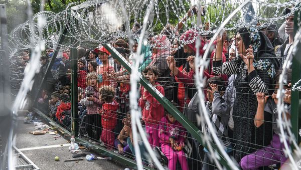 Refugees stand behind a fence at the Hungarian border with Serbia near the town of Horgos on September 16, 2015 - Sputnik International