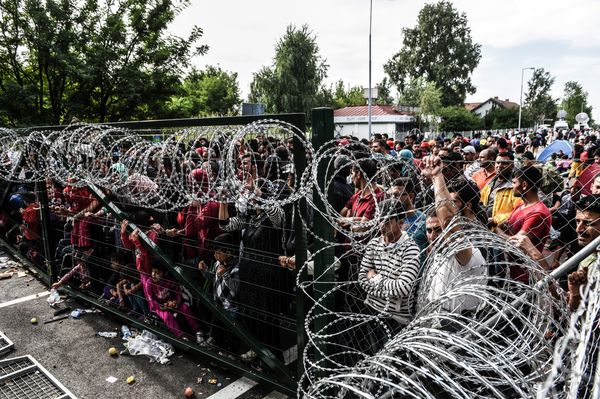 Refugees stand behind a fence at the Hungarian border with Serbia near the town of Horgos on September 16, 2015 - Sputnik International