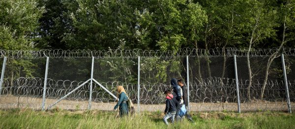 Migrants walk along the fence at the Serbian-Hungarian border while a helicopter flies over them near Horgos, Serbia,Tuesday, Sept. 15, 2015 - Sputnik International
