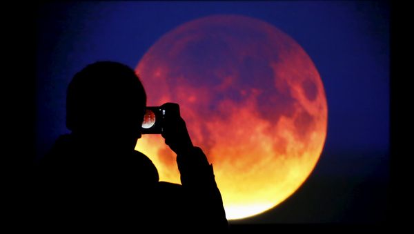 A man takes picture of the screen displaying the moon, appearing in a dim red colour, which is covered by the Earth's shadow during a total lunar eclipse in Warsaw, Poland September 28, 2015 - Sputnik International