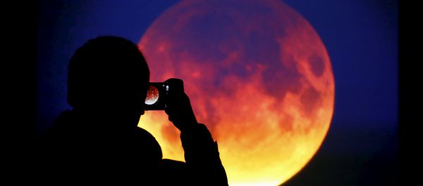 A man takes picture of the screen displaying the moon, appearing in a dim red colour, which is covered by the Earth's shadow during a total lunar eclipse in Warsaw, Poland September 28, 2015 - Sputnik International