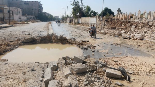 Residents ride a motorbike past a crater filled with water in Aleppo's al-Shaar neighborhood, Syria September 28, 2015 - Sputnik International