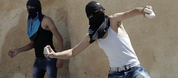 A masked Palestinian youth throws stones towards Israeli security forces during clashes - Sputnik International