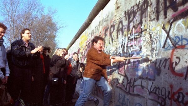 An unidentified West Berliner swings a sledgehammer, trying to destroy the Berlin Wall near Potsdamer Platz, on 12 November 1989, where a new passage was opened nearby - Sputnik International