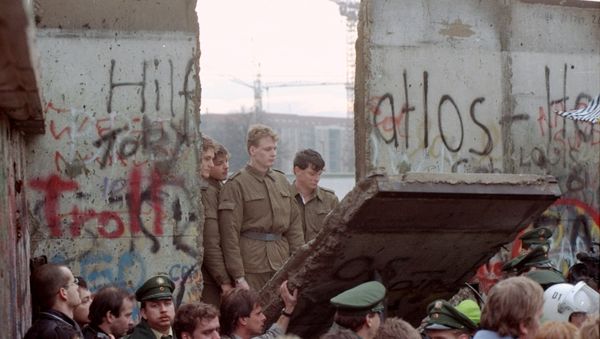 East German border guards look through a hole in the Berlin wall after demonstrators pulled down one segment of the wall at Brandenburg gate in this November 11, 1989 file picture - Sputnik International