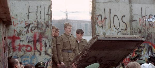 East German border guards look through a hole in the Berlin wall after demonstrators pulled down one segment of the wall at Brandenburg gate in this November 11, 1989 file picture - Sputnik International