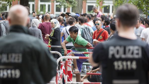 Police stand next to asylum seekers waiting in front of the reception center for refugees in Berlin, Germany, Friday, Aug. 7, 2015. Police stand next to asylum seekers waiting in front of the reception center for refugees in Berlin, Germany, Friday, Aug. 7, 2015. - Sputnik International