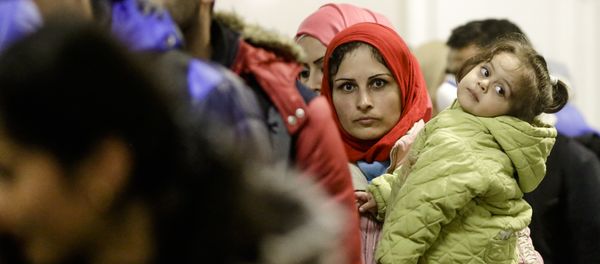 A migrant woman with a child stands in a queue of refugees and migrants after she arrived with a train at the train station Schoenefeld near, Berlin, Germany, Wednesday, Oct. 7, 2015. - Sputnik International