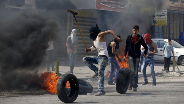 A Palestinian protester moves a burning tyre during clashes with the Israeli army at Qalandia checkpoint near occupied West Bank city of Ramallah October 6, 2015 - Sputnik International