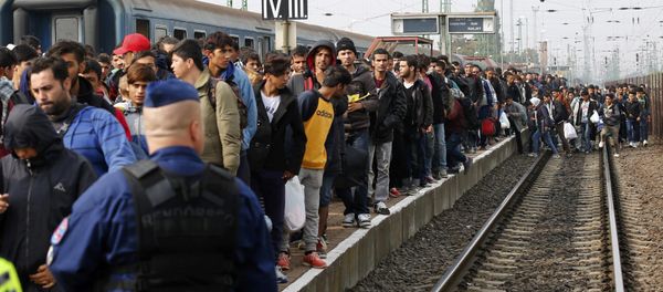 A Hungarian police officer watches as migrants arrive at the train station in Hegyeshalom, Hungary. File photo - Sputnik International