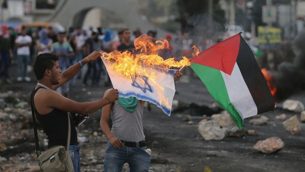 A protester burns a replica Israeli flag as another holds a Palestinian flag during clashes with the Israeli troops near the Jewish settlement of Bet El, near the West Bank city of Ramallah, 18 October 2015 - Sputnik International