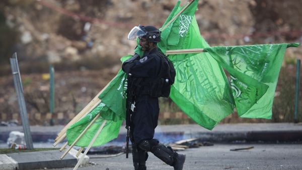 A member of the Israeli security forces carries flags of the Palestinian movement Hamas. - Sputnik International