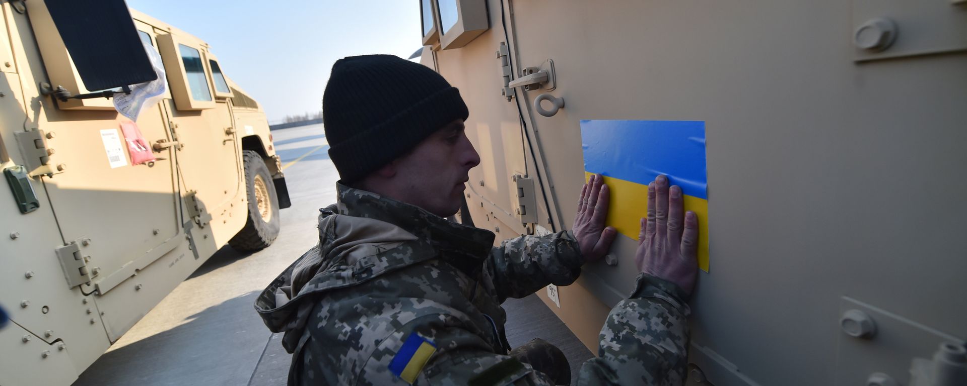 An Ukrainian serviceman sticks an Ukrainian flag on a Humvee at Kiev airport on March 25, 2015 during a welcoming ceremony of the first US plane delivery of non-lethal aid, including 10 Humvee vehicles - Sputnik International, 1920, 13.04.2022