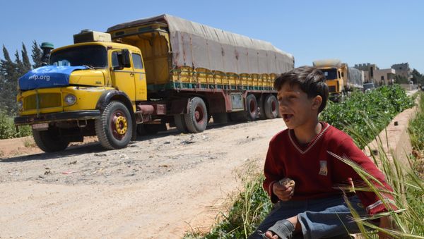 A Syrian child eats as he sits near a convoy of trucks from the World Food Programme and UNICEF carrying international aid as they drive in the countryside of the Homs district en route to the rebel held area of Al-Rastan north of the central Syrian city of Homs, on April 21, 2015. - Sputnik International