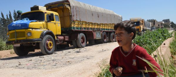 A Syrian child eats as he sits near a convoy of trucks from the World Food Programme and UNICEF carrying international aid as they drive in the countryside of the Homs district en route to the rebel held area of Al-Rastan north of the central Syrian city of Homs, on April 21, 2015. - Sputnik International