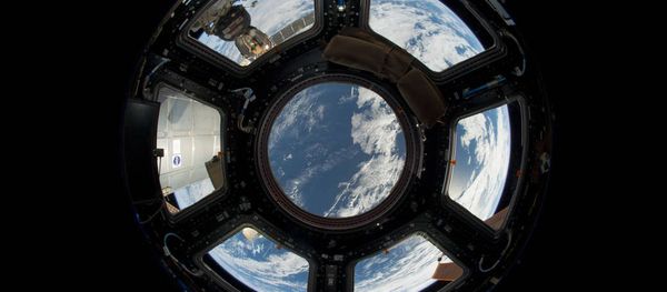 A view of Earth as seen from the Cupola on the Earth-facing side of the International Space Station. Visible in the top left foreground is a Russian Soyuz crew capsule. In the lower right corner, a solar array panel can be seen. - Sputnik International