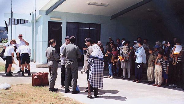 This file photo taken on August 19, 2001 shows officials (C-in green flight uniforms) questioning a refugee as other refugees (R), mostly believed to be from Iraq, wait in the shade before boarding an Australian Air Force Hercules aircraft on the Australian island territory of Christmas Island in the Indian Ocean. - Sputnik International