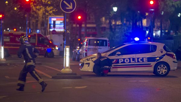 A police officer takes cover behind a car while a rescue worker runs outside the Bataclan theater in Paris, France, Wednesday, Nov. 13, 2015. - Sputnik International