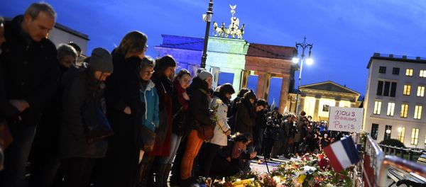 A banner reading 'We are Paris ' is pictured among candles and flowers in front of the Brandenbourg Gate outside the French embassy in Berlin, on November 14, 2015 a day after deadly attacks in Paris - Sputnik International