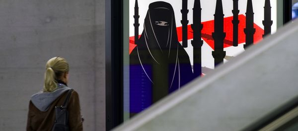 A woman passes by a campaign poster of the far-right Swiss People's Party depicting a woman wearing a burqa against a background of a Swiss flag upon which several minarets resembling missiles on October 26, 2009 at the central station in Zurich. - Sputnik International