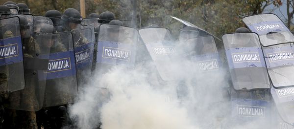 Macedonian police officers try to take cover from tear gas thrown back by a stranded migrant, as minor clashes broke out during a protest against the building of a metal fence at the Greek-Macedonian borders near the village of Idomeni, Greece November 28, 2015 - Sputnik International