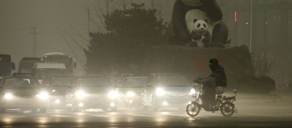 A resident rides an electric bicycle across a street amid heavy smog as vehicles wait for a traffic light next to a statue of pandas, a landmark of the Wangjing area in Beijing, China, December 1, 2015 - Sputnik International