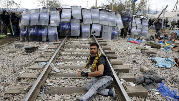 A stranded migrant reacts in front of a Macedonian police cordon as they clash after a migrant was injured when he climbed on top of a train wagon, near the village of Idomeni, Greece, November 28, 2015. A stranded migrant reacts in front of a Macedonian police cordon as they clash after a migrant was injured when he climbed on top of a train wagon, near the village of Idomeni, Greece, November 28, 2015. - Sputnik International